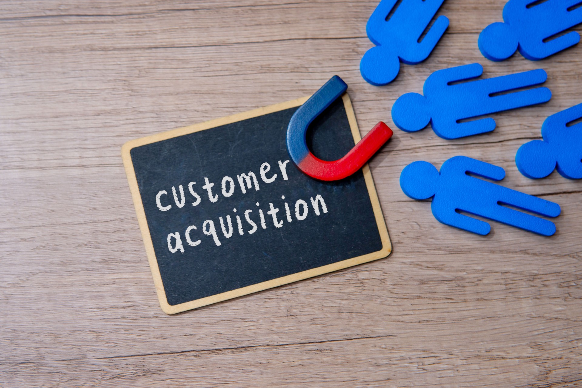 A chalkboard with the words CUSTOMER ACQUISITION and magnet attract customer.
